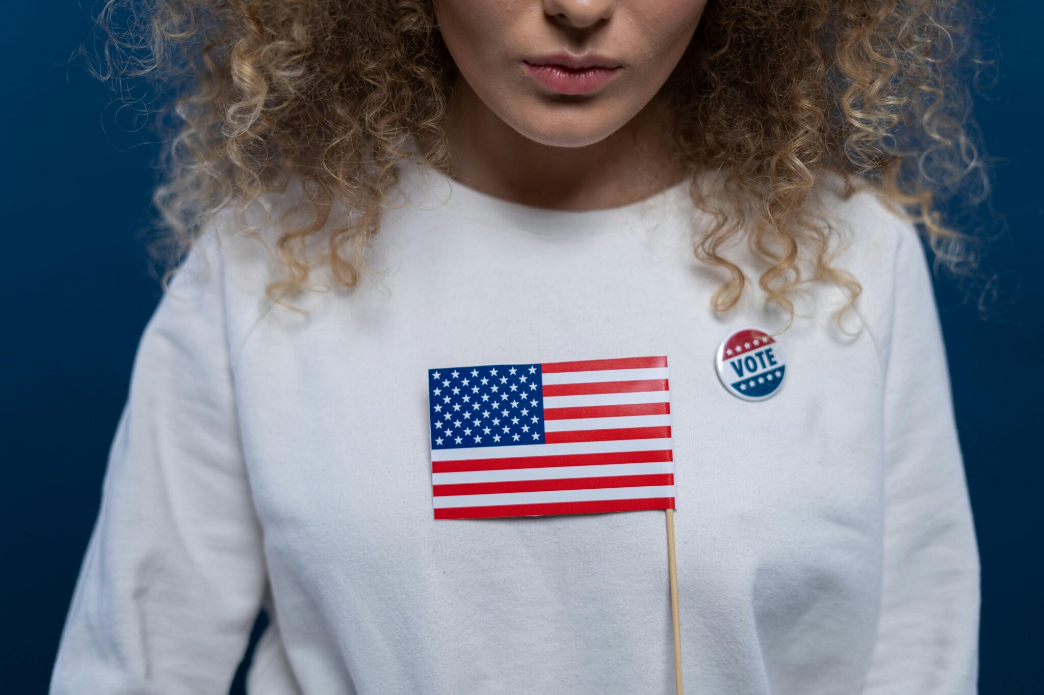 A woman with curly hair wearing a white shirt and holding an american flag.