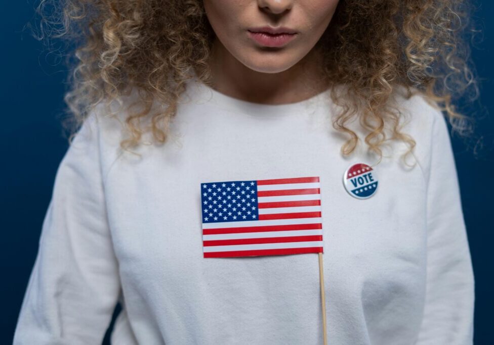 A woman with curly hair wearing a white shirt and holding an american flag.