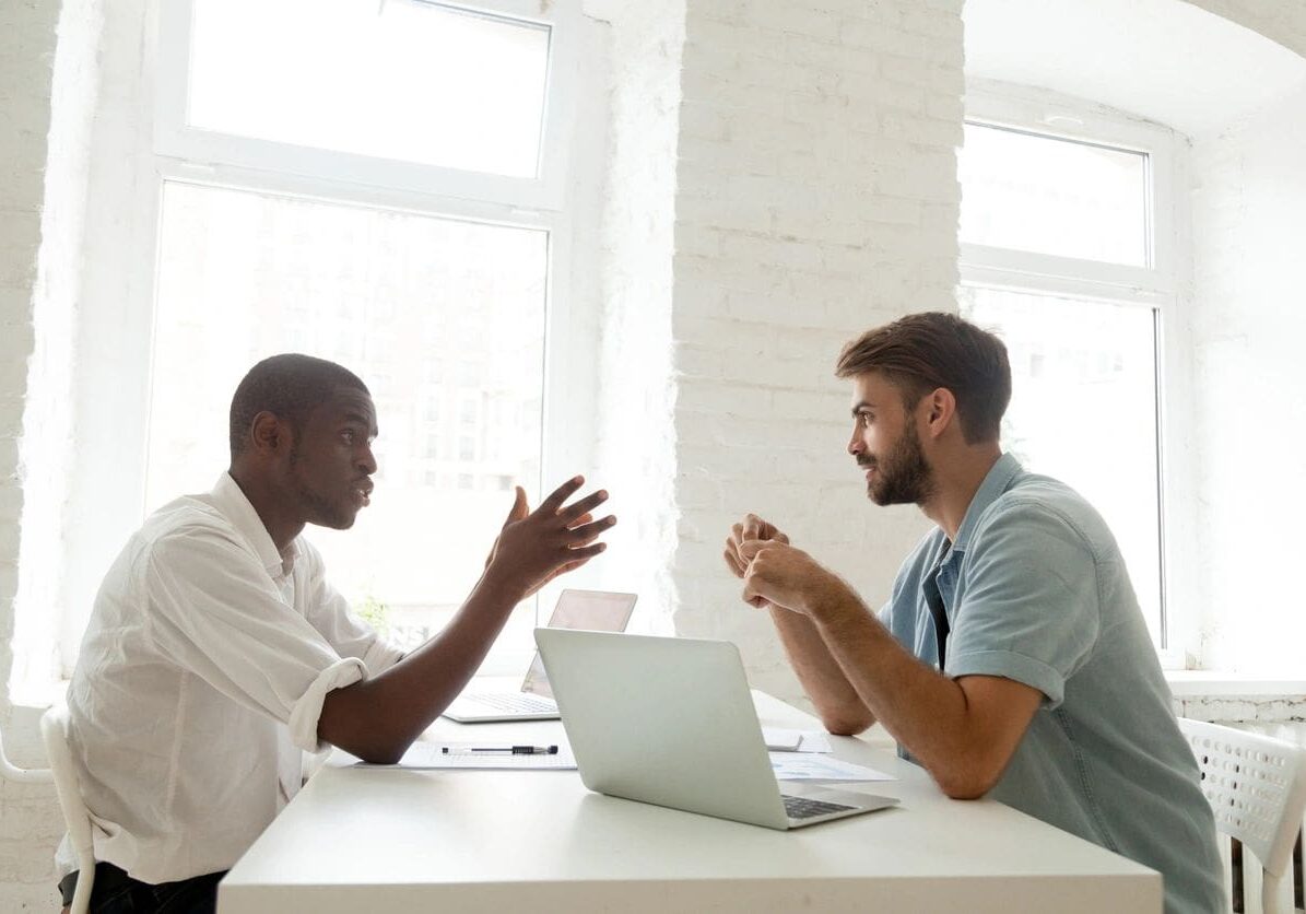 Two men sitting at a table with laptops